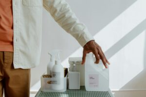 Close-up of a man holding fabric softener surrounded by cleaning products in a minimalist setting.